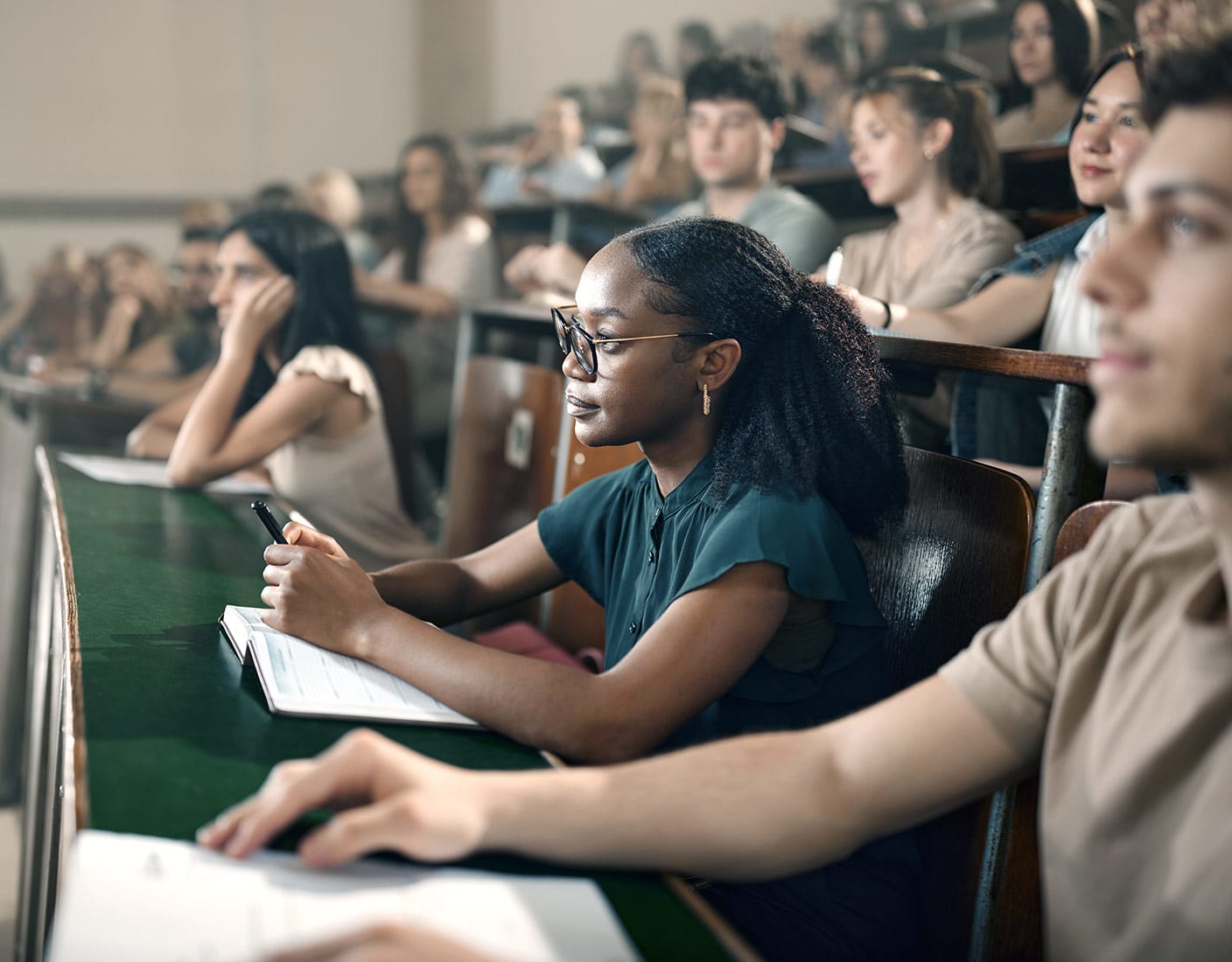 A diverse group of people attentively seated in a lecture hall, facing a speaker at the front.